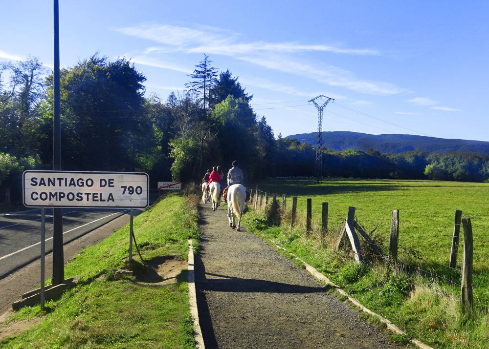 personas a caballo saliendo de Roncevalles y cartel con los kms que quedan hasta Santiago